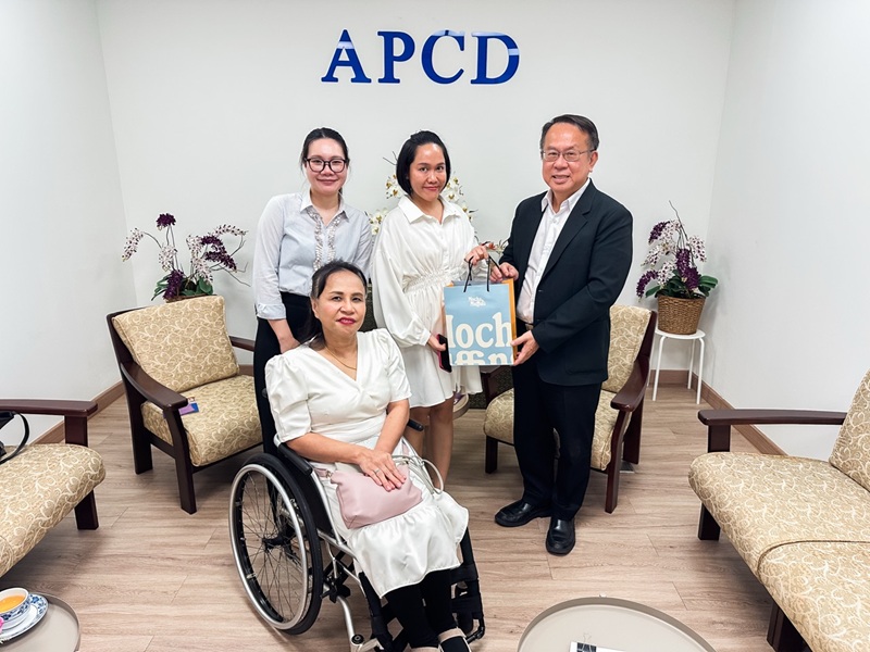 Picture 1: From left to right, Ms. Nitwari Sikon, Ms. Kingkarn Siriwat (left) and Mr. Piroon Laismit (right), both holding a gift together and Ms. Nongnuch Maytarjittipun (seated in a wheelchair in front of Ms. Nitwari Sikon)
