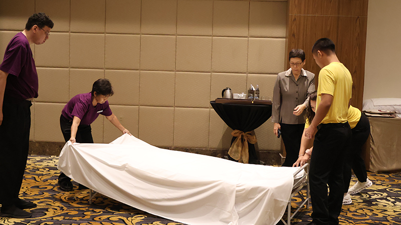 Picture 4: Two trainees in purple T-shirts (left) and one trainee in yellow T-shirt (right) demonstrating bed making.