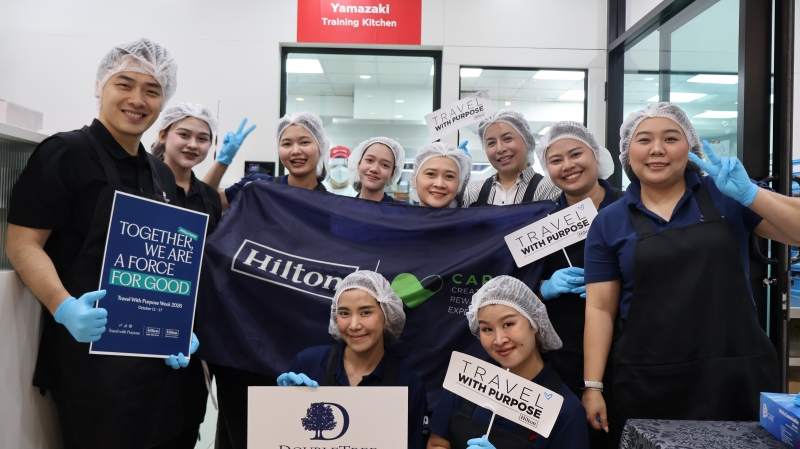 Representatives from DoubleTree by Hilton Bangkok Ploenchit hold a 'Travel with Purpose' sign while posing for a photo before a bakery workshop session.