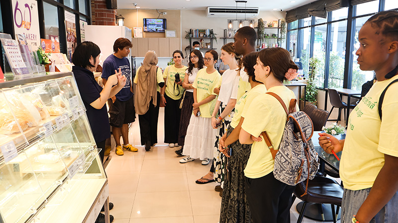 รูปที่ 5: นางสาวศุภอนงค์ ปัญญาสิริมงคล นำคณะนักศึกษาเข้าเยี่ยมชมโครงการร้าน 60+ Plus Bakery & Café และโครการ "การพัฒนาศักยภาพคนพิการ" รวมถึงครัว APCD 60+ Plus Kitchen by CP
