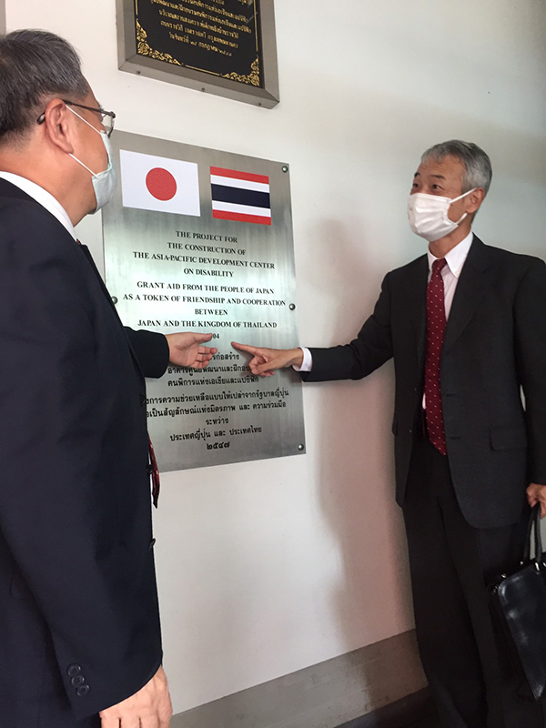 Photo of Mr. Morita and Mr. Piroon in front of a symbol of relationship between Thailand and Japan.