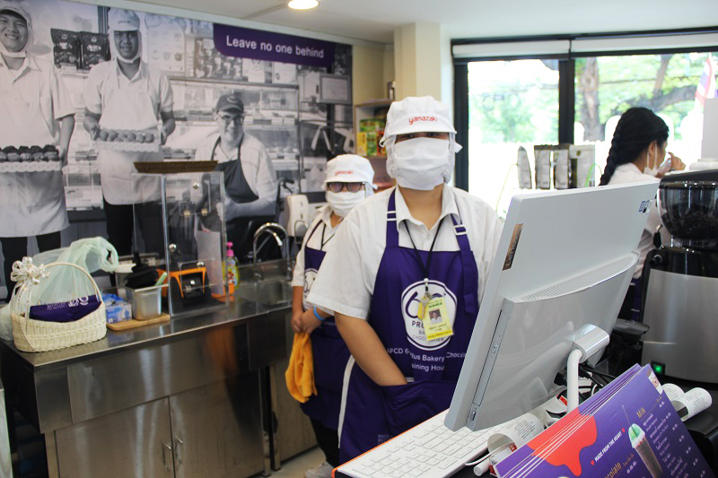 Trainees with disabilities and cafe staff wear face masks and aprons made from recycled materials.