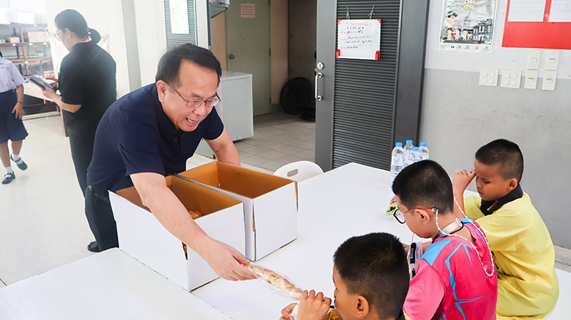 Picture 6: Mr. Piroon Laismit, Executive Director of APCD, distributes wrapped pieces of bread from donation boxes to students in the cafeteria.