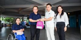 Picture 1: Participants pose for a group photo. Mr. Piroon Laismit and Mr. Asdang Sukwises hold souvenirs, while Ms. Nongnuch Maytarjittipun is seated in a wheelchair on the left side of the group