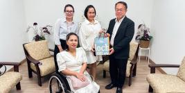 Picture 1: From left to right, Ms. Nitwari Sikon, Ms. Kingkarn Siriwat (left) and Mr. Piroon Laismit (right), both holding a gift together and Ms. Nongnuch Maytarjittipun (seated in a wheelchair in front of Ms. Nitwari Sikon)
